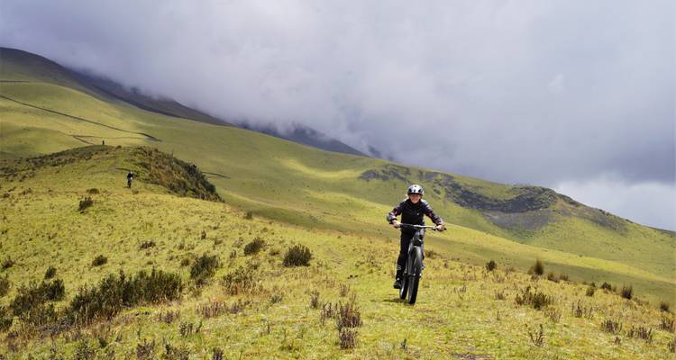 Radfahrer, der über offene Hochgebirgsgrasland unter einem düsteren bewölkten Himmel fährt