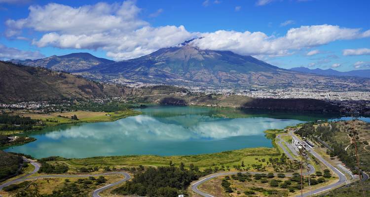Smaragdgrüner See, der Wolken und die umliegenden Berge widerspiegelt, mit einer Stadt, die sich an seinem Ufer ausbreitet