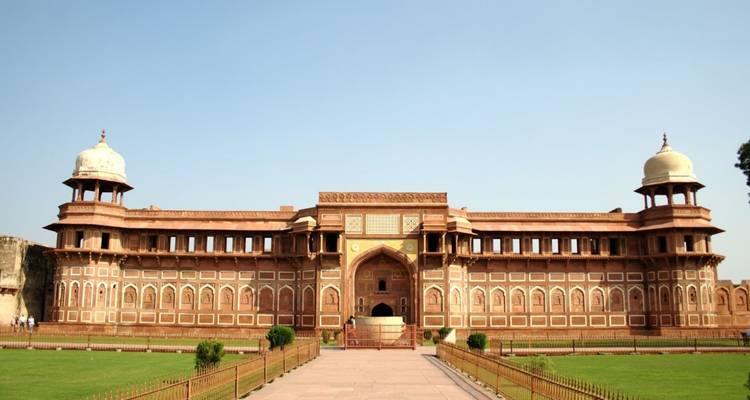 Lange symmetrische Fassade des Palastes aus rotem Sandstein im Agra Fort, eingerahmt von gepflegten Rasenflächen und blauem Himmel.