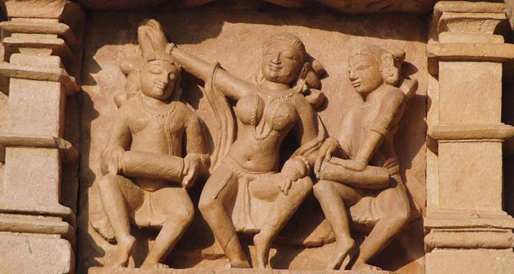 Nahaufnahme einer Khajuraho-Sandsteinschnitzerei, die drei Musiker in dynamischen Posen zeigt.