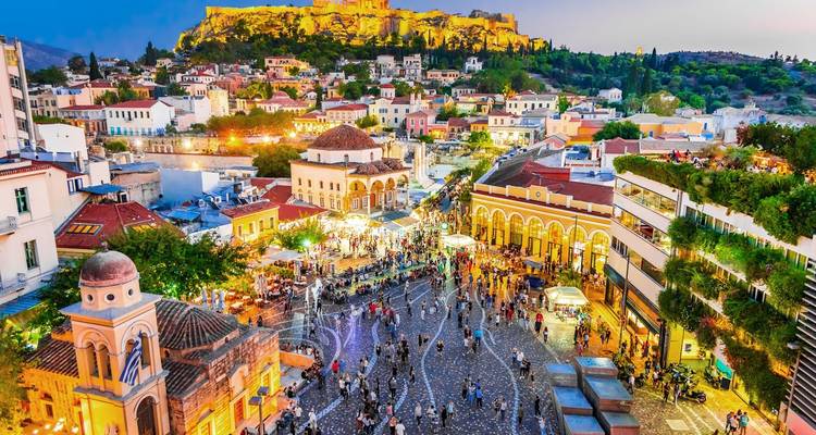Levendige avondscène van het Monastiraki-plein met drukke menigten en de verlichte Akropolis op de achtergrond.