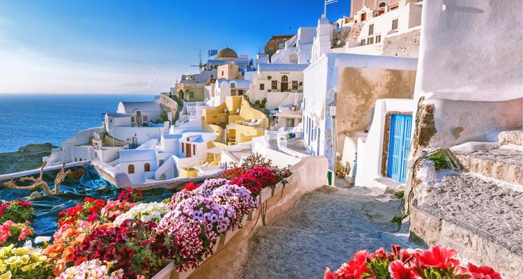 Charmante met bloemen omzoomde steeg van Oia met pastelkleurige huizen die naar de diepblauwe zee afdalen.