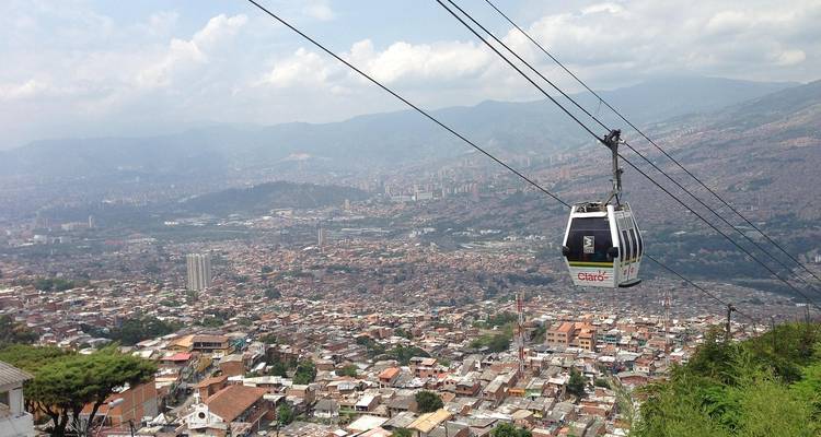 Una cabina de góndola del sistema de teleférico urbano se desliza sobre una extensa ciudad montañosa bajo cielos brumosos.