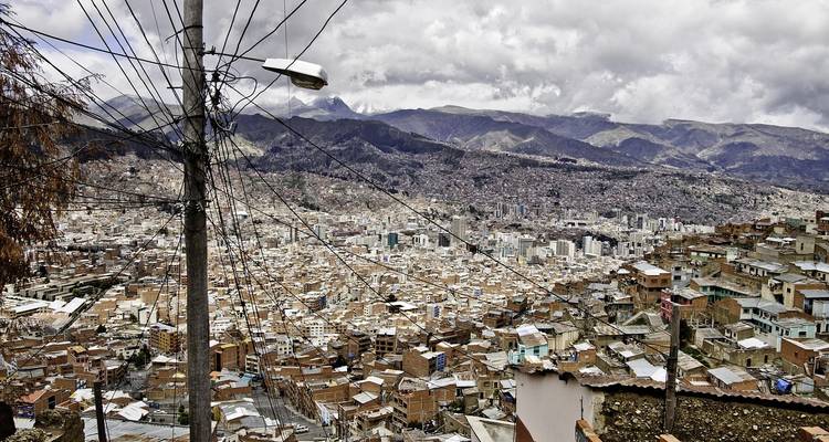 Expansión en la ladera de La Paz vista a través de una red de cables eléctricos bajo nubes espesas.