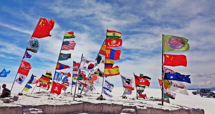 Banderas internacionales brillantes ondean en la cima de un pedestal de sal en el vasto Salar de Uyuni blanco.