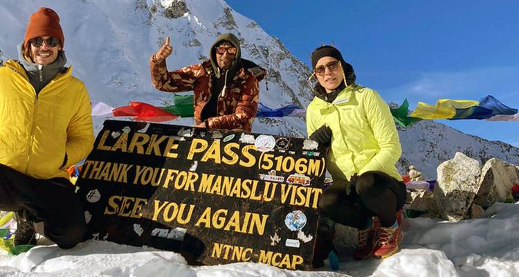 Trekkers poseren bij het Larke Pass 5106 m bord temidden van besneeuwde bergtoppen en gebedsvlaggen.