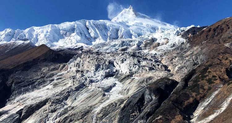 De met sneeuw bedekte Mount Manaslu rijst kaal op boven gebarsten gletsjers en rotsachtige bergkammen.