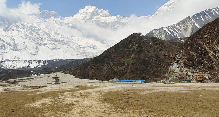Open alpenweide onder torenhoge besneeuwde Himalaya-toppen met verspreide gebedsbouwwerken.