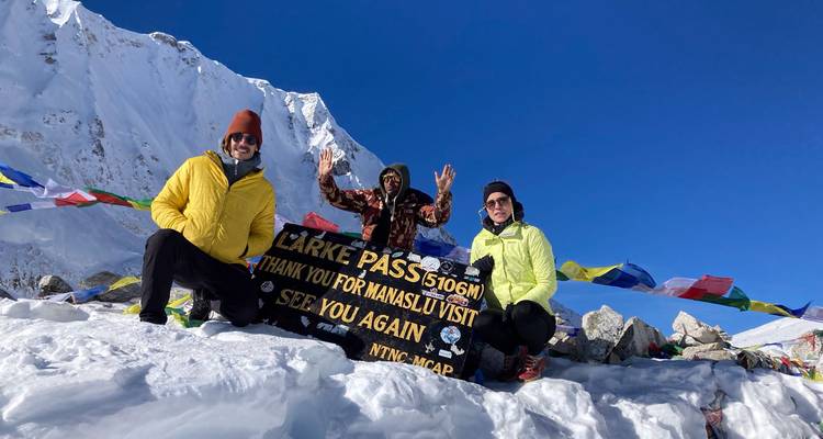 Groep viert bij het Larke Pass-topbord omringd door kleurrijke gebedsvlaggen en sneeuw.