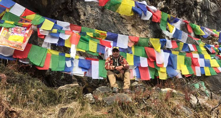 Trekker rust op een rotsblok bedekt met veelkleurige gebedsvlaggen naast een klif.