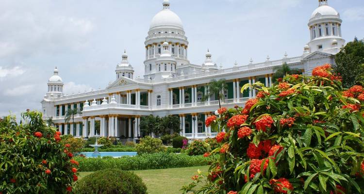 Eleganter weißkuppeliger Lalitha Mahal Palast, eingerahmt von blühenden roten Blumen und gepflegten Gärten.