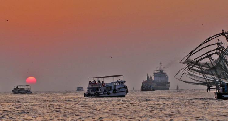 Orangene Sonne geht über dem Arabischen Meer unter, während Ausflugsboote und chinesische Fischernetze den Horizont silhouettieren.