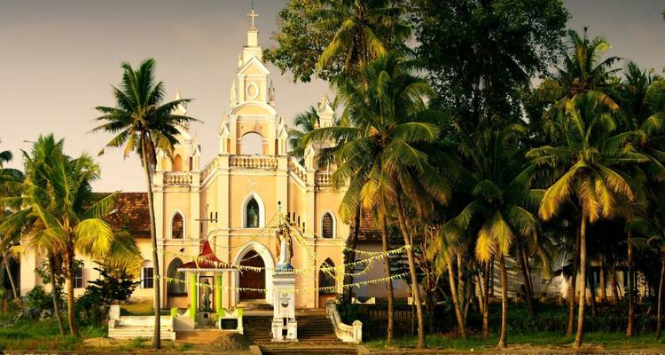 Cremefarbene Kirche mit Zwillingstürmen eingebettet zwischen üppigen Palmen entlang der Backwaters von Kerala.