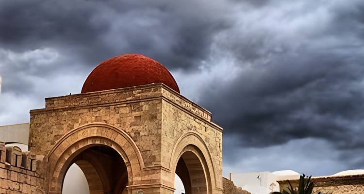 Une arche de pierre surmontée d'un dôme rouge saisissant se dresse contre des nuages d'orage dramatiques.