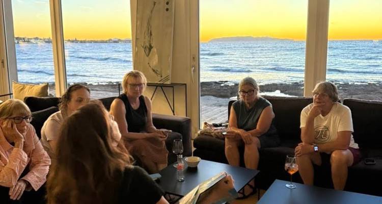 Petit groupe se détendant sur des canapés à l'intérieur tout en profitant de la vue du coucher de soleil sur l'océan à travers de grandes fenêtres