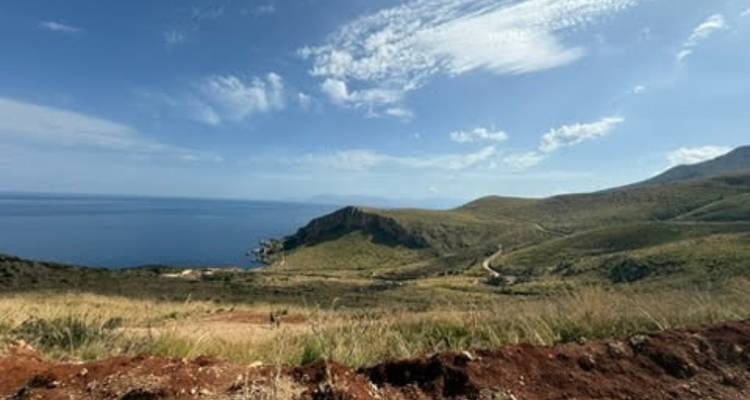 Vaste paysage côtier avec des collines ondulantes, une route sinueuse et une mer d'un bleu profond sous un ciel lumineux