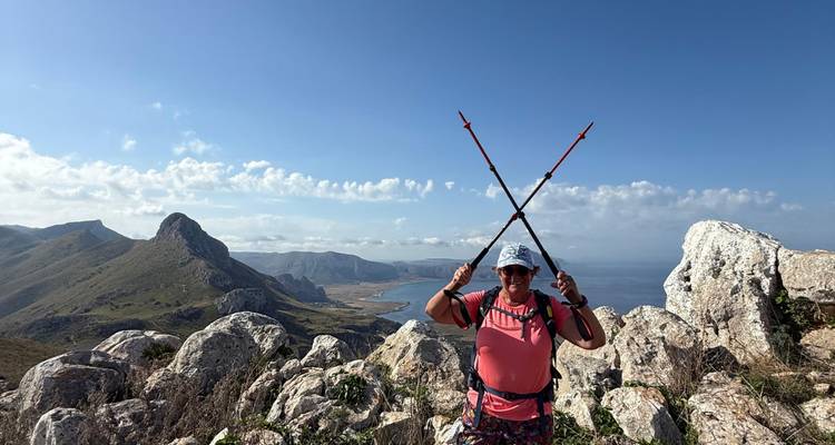 Randonneur souriant tenant des bâtons de randonnée croisés sur une crête rocheuse surplombant un littoral spectaculaire