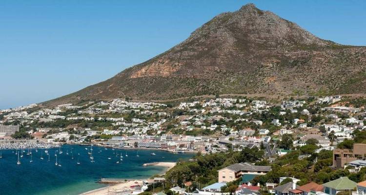 Vue panoramique d'une ville côtière et d'un port de plaisance au pied d'une montagne conique escarpée sous un ciel bleu éclatant.
