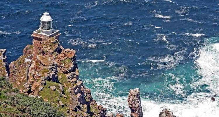 Phare historique perché sur une falaise déchiquetée au-dessus des vagues tourbillonnantes d'un océan bleu profond.