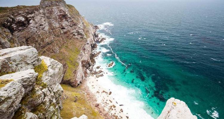 Promontoire rocheux spectaculaire plongeant vers une eau turquoise et une petite crique de sable blanc.