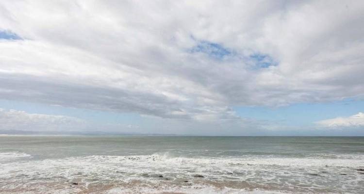 Vue large d'un océan gris calme sous un ciel majoritairement nuageux.