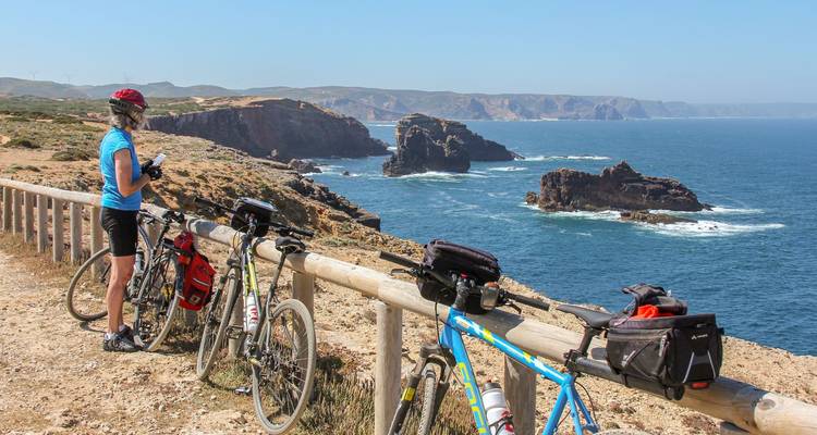 Radfahrer macht eine Pause an einem Holzgeländer mit Blick auf zerklüftete Meeresklippen und den Atlantischen Ozean.