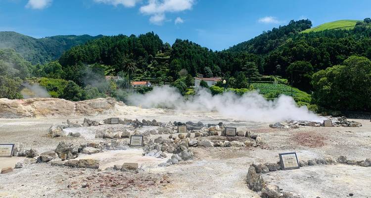 Dampfende geothermische Felder von Furnas mit bewaldeten Hügeln, die hinter Schwefelquellen aufragen.