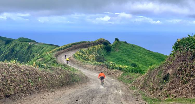 Mountainbiker fährt einen staubigen Klippenpfad mit weiten Atlantikblicken auf São Miguel hinab.