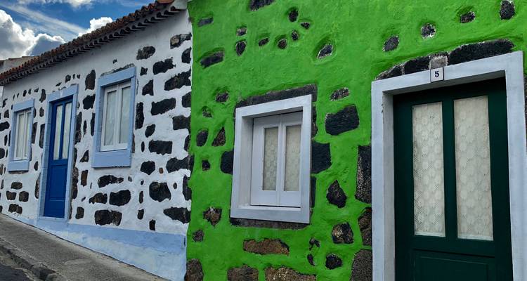 Traditionelle azorianische Häuser mit schwarzem Lavagestein und leuchtend bemalten Türen entlang einer Dorfgasse.