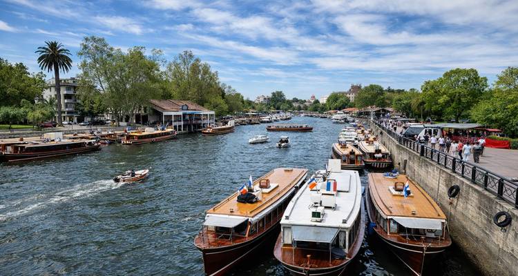 Port fluvial animé avec des bateaux d'excursion en bois classiques, des palmiers et des gens se promenant le long du quai sous un ciel bleu.