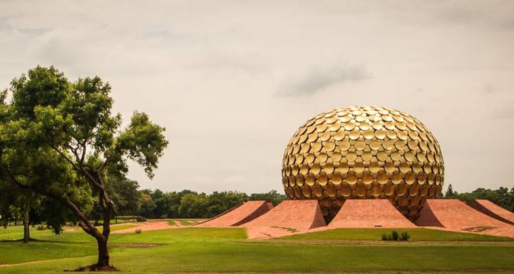 Die goldene Matrimandir-Kugel, die sich über gepflegten Rasenflächen unter einem dunsigen Himmel in Auroville erhebt.