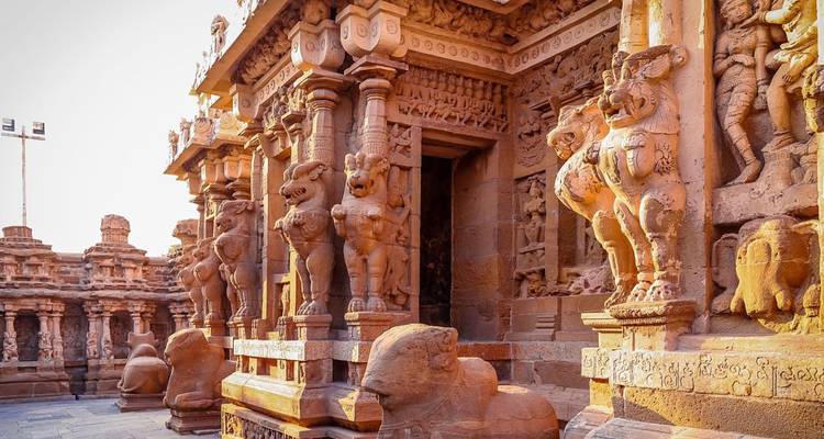 Sonnenbeschienener Korridor eines kunstvollen Tempels aus der Chola-Zeit, geschmückt mit geschnitzten Säulen und steinernen Stieren.