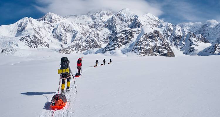 Des alpinistes traversant une vaste étendue enneigée vers l'imposant sommet du Denali sous un ciel bleu cristallin.