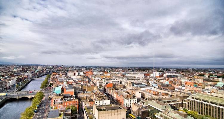 High aerial panorama of Dublin city showing the River Liffey and dense urban landscape under gray clouds.