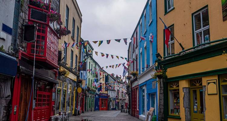 A narrow pedestrian street in Galway lined with colorful facades and festive bunting on an overcast day.