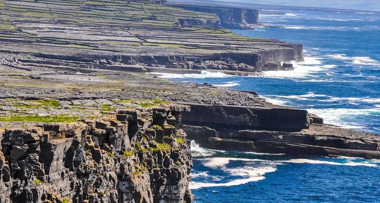 Dramatische terrassenförmige Kalksteinklippen fallen steil ab zu einem tiefblauen Atlantik, während weiße Brandung gegen die Küste der Aran-Inseln kracht.