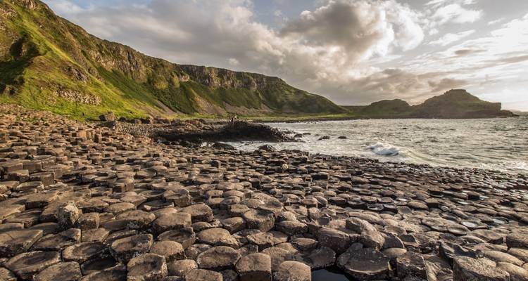Sechseckige Basaltsäulen bilden die unwirkliche Küstenlinie des Giant's Causeway unter grünen Klippen und dramatischen Wolken.