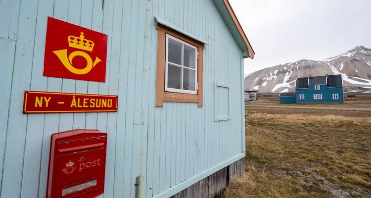 Lichtblauw houten postkantoorgebouw met Ny-Ålesund bord en arctische bergen op de achtergrond.