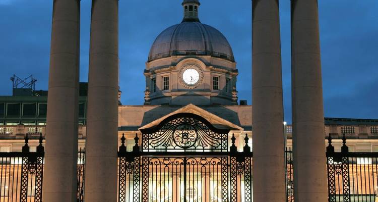 Verlichte neoklassieke koepel en klokkentoren omlijst door stenen zuilen bij schemering in Dublin.