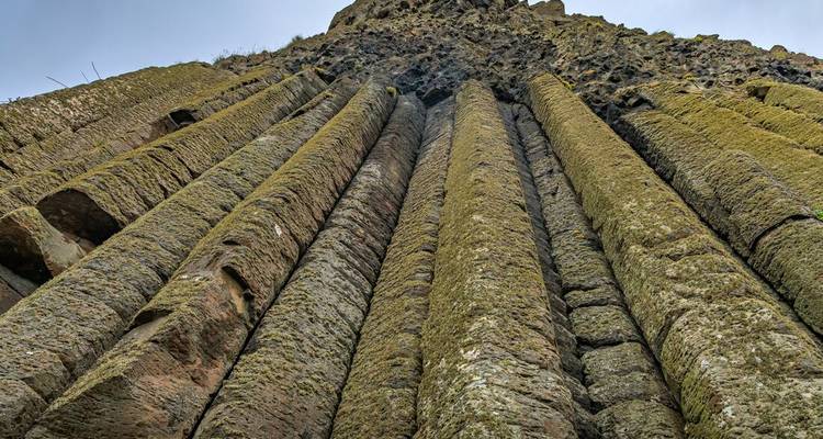 Omhooggaande close-up van met mos bedekte basaltkolommen die een dramatische natuurlijke muur vormen.