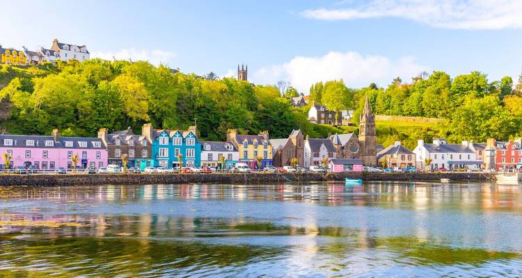 Rij pastelkleurige huizen aan de waterkant en kerktoren die reflecteren in de haven van Tobermory.