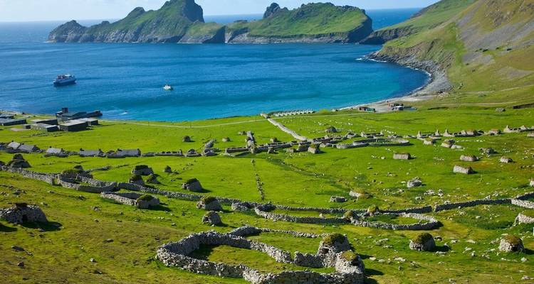 Blauwe baai en groene weiden bezaaid met stenen ruïnes in het afgelegen St. Kilda eilanddorp.