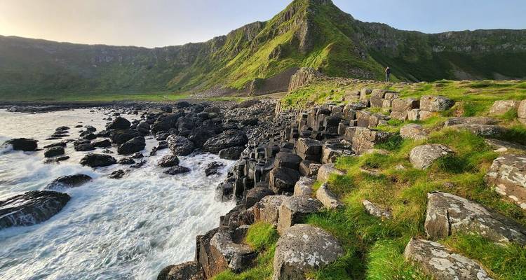 Eenzame bezoeker staat tussen basaltzuilen en beukende golven aan de kust van Giant's Causeway.