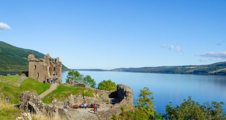 Ruïnes van Urquhart Castle kijken uit over de stille blauwe wateren van Loch Ness met bezoekers die aan het verkennen zijn.