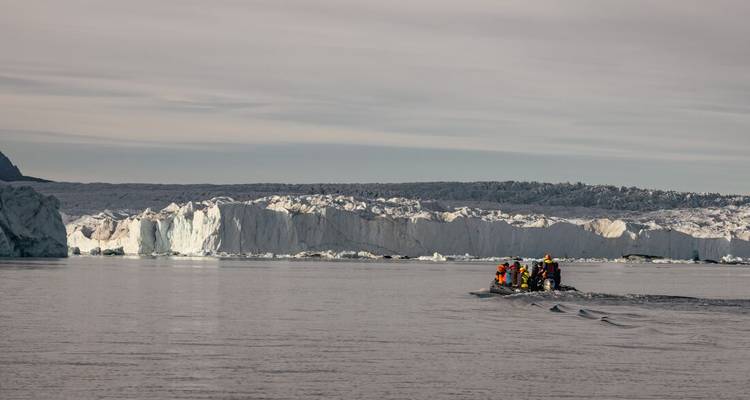 Bateau zodiac de voyageurs groupés s'approche d'un glacier blanc imposant à travers les eaux calmes de l'Arctique.