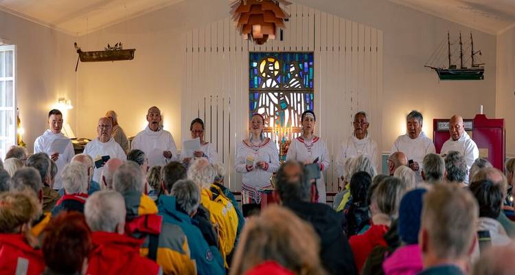 Une chorale locale chante dans une petite église groenlandaise remplie d'invités d'expédition en vestes.