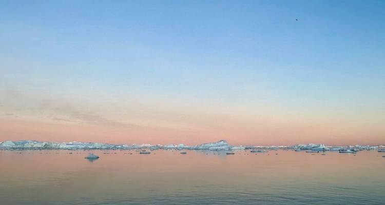 Coucher de soleil rose pastel et bleu sur une mer parsemée d'icebergs lointains.