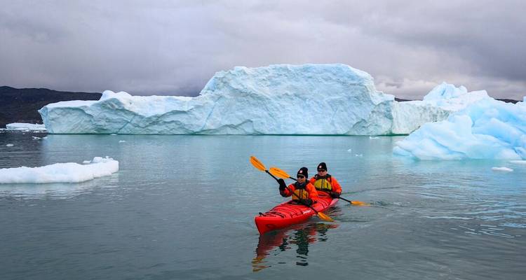 Deux kayakistes pagaient dans un kayak rouge parmi d'énormes icebergs bleus sur une eau calme.