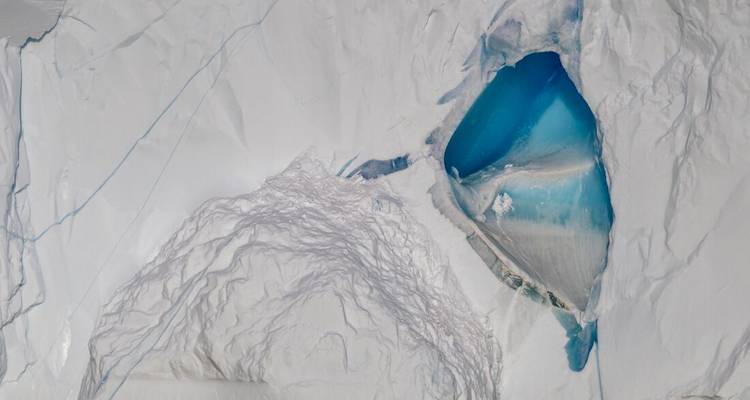 Vue aérienne d'un glacier crevassé révélant un bassin d'eau de fonte d'un bleu saisissant.