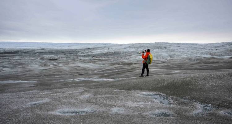 Voyageur solitaire avec appareil photo se tient sur la vaste surface grise de la calotte glaciaire du Groenland.